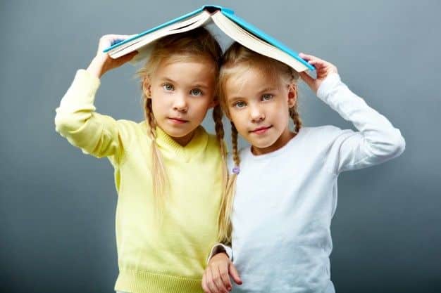 hermanas-usando-un-libro-abierto-como-un-paraguas_1098-3777