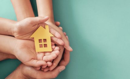 Manos sujetando figura de una casa en papel