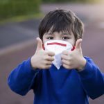Niño con mascarilla hace el signo de todo ok con los pulgares hacia arriba