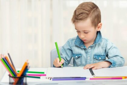 un niño escribe a mano con un lapicero de color verde