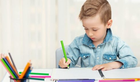 un niño escribe a mano con un lapicero de color verde