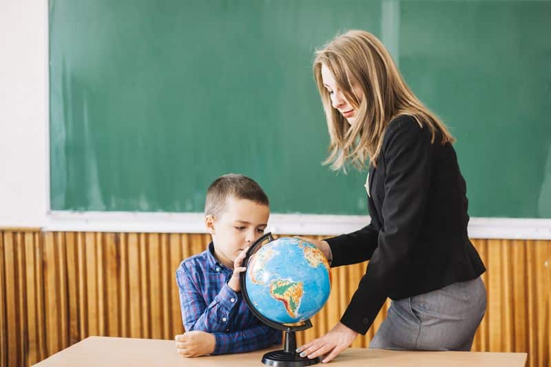 Un Niño Se Concentra Mientras Mira La Bola Del Mundo Con Su Profesora