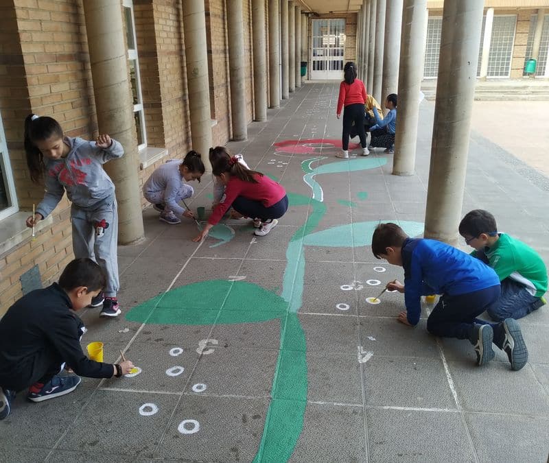 Los alumnos pintan en el suelo del patio una flor entre todos