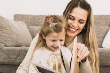 cheerful mother and daughter reading book near sofa